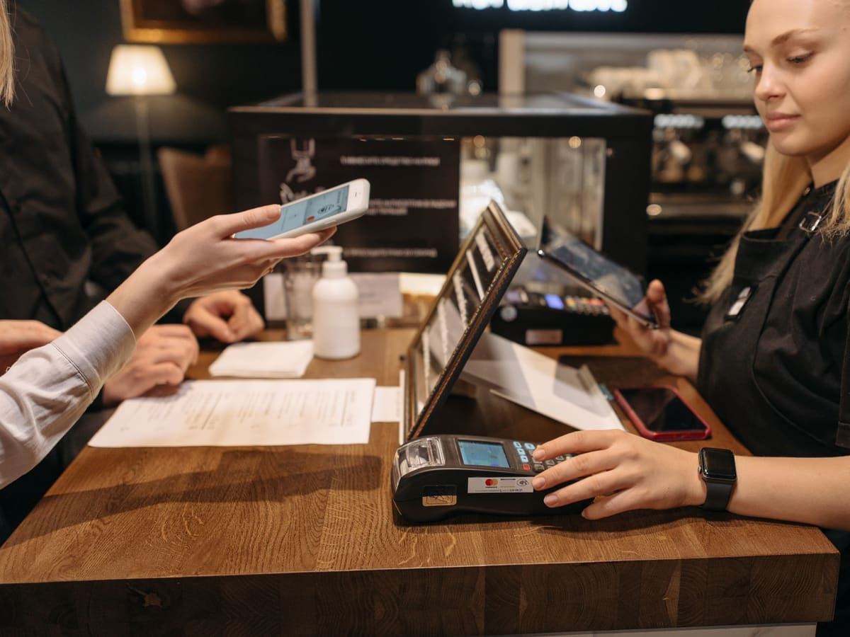 A customer holding her phone to the payment terminal at a café counter.